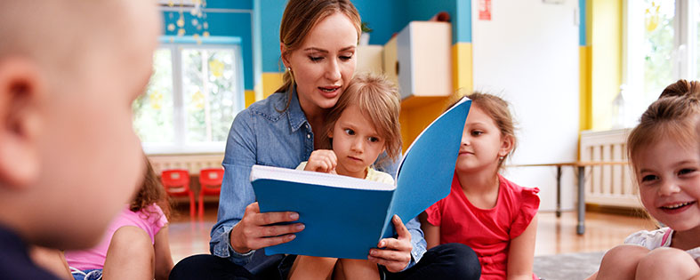 teacher reading to young children out of a blue book